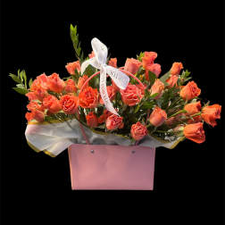Coral roses arranged in a pink gift box with a ribbon bow