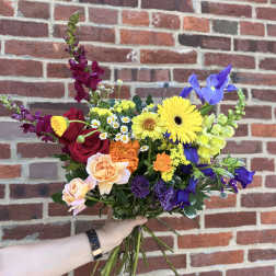 Colorful hand-tied bouquet with yellow gerbera daisies, red roses, purple irises, and assorted mixed flowers