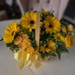 Yellow gerbera daisies and roses in a small basket with a ribbon