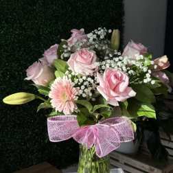 Pink roses and a gerbera daisy in a glass vase with a pink bow