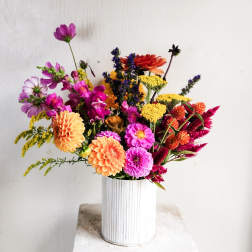 Mixed bouquet of orange, pink, yellow, and purple flowers in a white vase