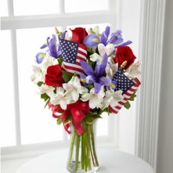 Bouquet of red roses and purple flowers with small American flags in a glass vase