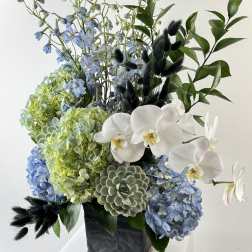 Blue and green floral arrangement with white orchids in a black vase