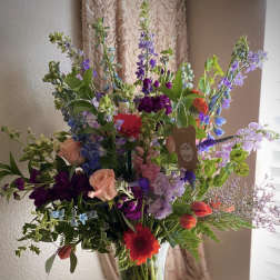 Tall mixed arrangement of colorful roses, tulips, gerbera daisies and other blooms in a clear glass vase