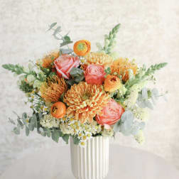 Peach and orange mixed flower arrangement with roses and ranunculus in a tall white ceramic vase
