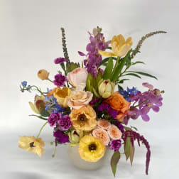Colorful mixed bouquet in a white vase with orchids and roses