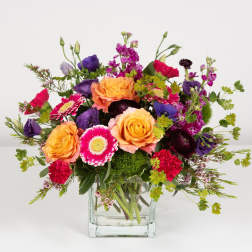 Mixed bouquet of orange, pink, and purple flowers in a clear glass vase