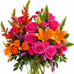 Bright mixed bouquet of pink roses, orange lilies, and orange snapdragons in a glass vase