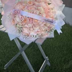 Large bouquet of pale pink roses wrapped in pink paper with a ribbon