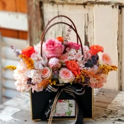 Pink and orange roses arranged in a black gift box with a handle