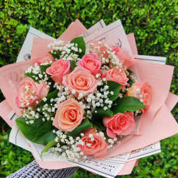 Hand-tied bouquet of peach roses and white filler flowers wrapped in pink paper