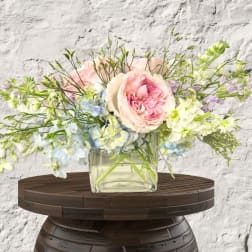 Pastel bouquet of pink roses and blue-white flowers in a clear glass vase