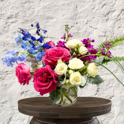 Bouquet of pink and white roses with blue and purple flowers in a glass vase