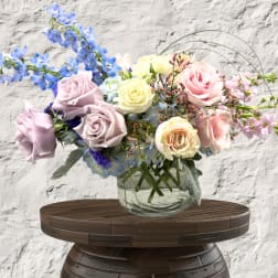 Pastel roses and blue flowers arranged in a clear glass vase