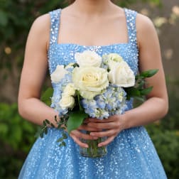 Woman in a blue dress holding a bouquet of white roses and blue hydrangeas in a glass vase
