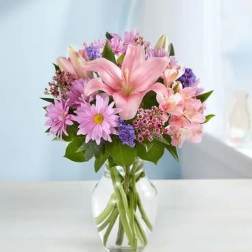 Pink lilies and purple daisies in a clear glass vase