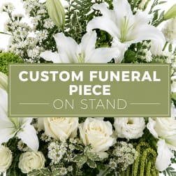 White lilies and roses arranged around a funeral sign on a stand