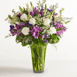 Bouquet of white roses and purple flowers in a tall glass vase