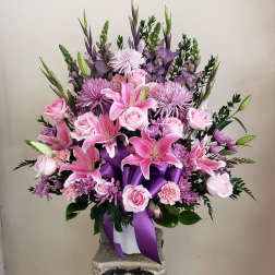 Pink and purple floral arrangement in a white container with a purple ribbon