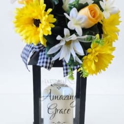 Yellow and white floral arrangement in a black lantern with a candle