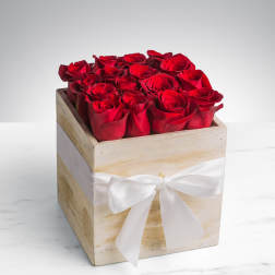 Square arrangement of red roses in a rustic wooden box with a white ribbon bow