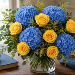 Blue hydrangeas and yellow roses in a clear glass vase