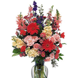 Mixed bouquet of red, pink, yellow, and purple flowers in a glass vase