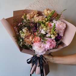 Hand-tied bouquet of pink and peach flowers wrapped in blush paper