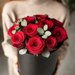 Red roses arranged in a black hat box with eucalyptus