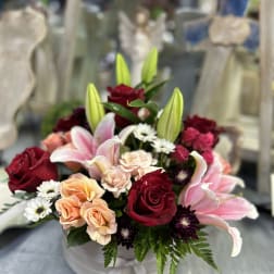 Mixed bouquet of red roses, pink lilies, and peach spray roses in a white hatbox