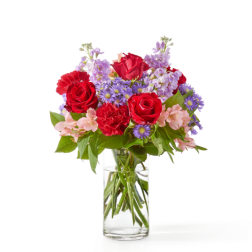 Mixed bouquet of red roses and carnations with purple and pink blooms in a clear glass vase