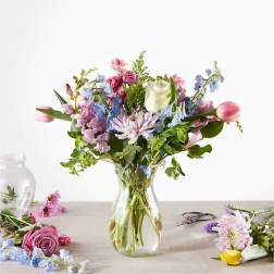 Mixed bouquet of pink, blue, and white flowers in a clear glass vase