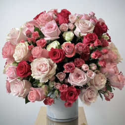 Rounded arrangement of pink and red roses in a white ceramic cylinder vase