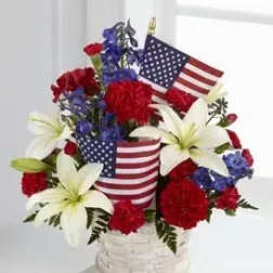Red, white, and blue floral arrangement in a white basket with American flags