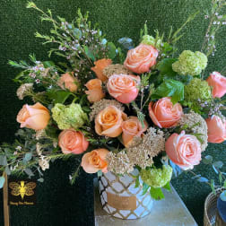 Peach rose arrangement with green blooms in a patterned white container.