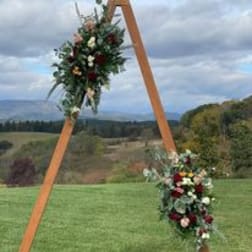 Two floral arrangements on a wooden arch outdoors