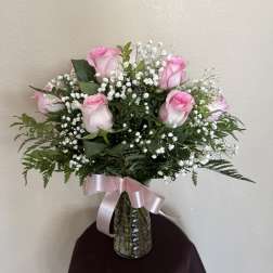 Pink roses and baby's breath in a glass vase with a pink ribbon