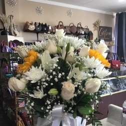 Large white and yellow flower arrangement in a glass vase with a white ribbon