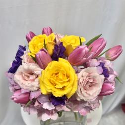 Bouquet of yellow roses, pink tulips, and pale pink flowers in a glass vase