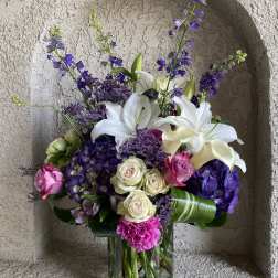 Bouquet of white lilies, purple flowers, and pink roses in a glass vase