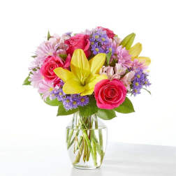 Bright bouquet of yellow lilies, pink roses, and purple daisies in a clear glass vase