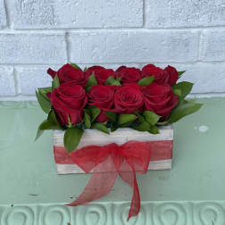 Red roses arranged in a rustic wooden box with a red ribbon