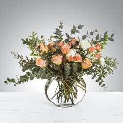 Peach and white roses in a round glass vase with eucalyptus