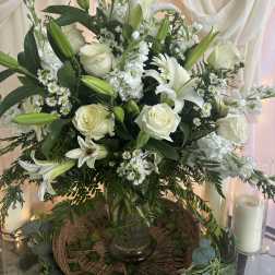 White lilies and roses arranged in a glass vase with greenery