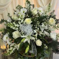 White roses and daisies arranged in a basket with a sheer ribbon