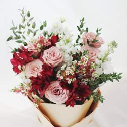Bouquet of pink roses, red flowers, and white blooms wrapped in gold paper