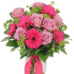 Pink roses and gerbera daisies in a glass vase with a pink ribbon