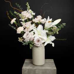 White lilies and pale roses in a tall vase with curly branches