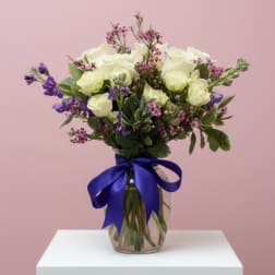 White and purple flower bouquet in a glass vase with a blue ribbon