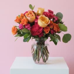 Bouquet of orange, yellow, and pink roses in a clear glass vase